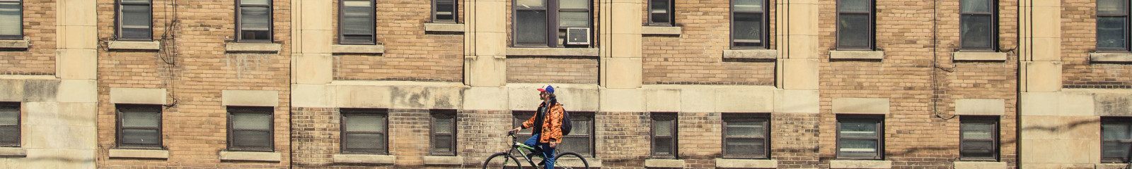 man on bike in front of an old brick apartment building